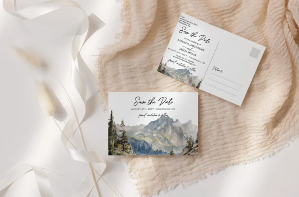 Paperlust destination wedding save the date postcard with hand-painted mountain illustration and matching RSVP card on a cream linen surface with dried wheat styling.
