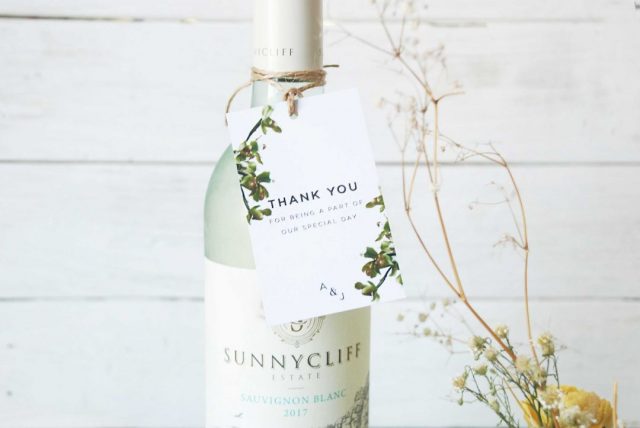 Paperlust thank you gift tag tied with jute twine to a wine bottle wedding favor, styled with dried flowers on white timber