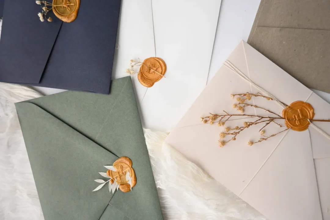 Styled wedding invitation envelopes in sage, navy, blush and kraft with gold wax seals, Paperlust