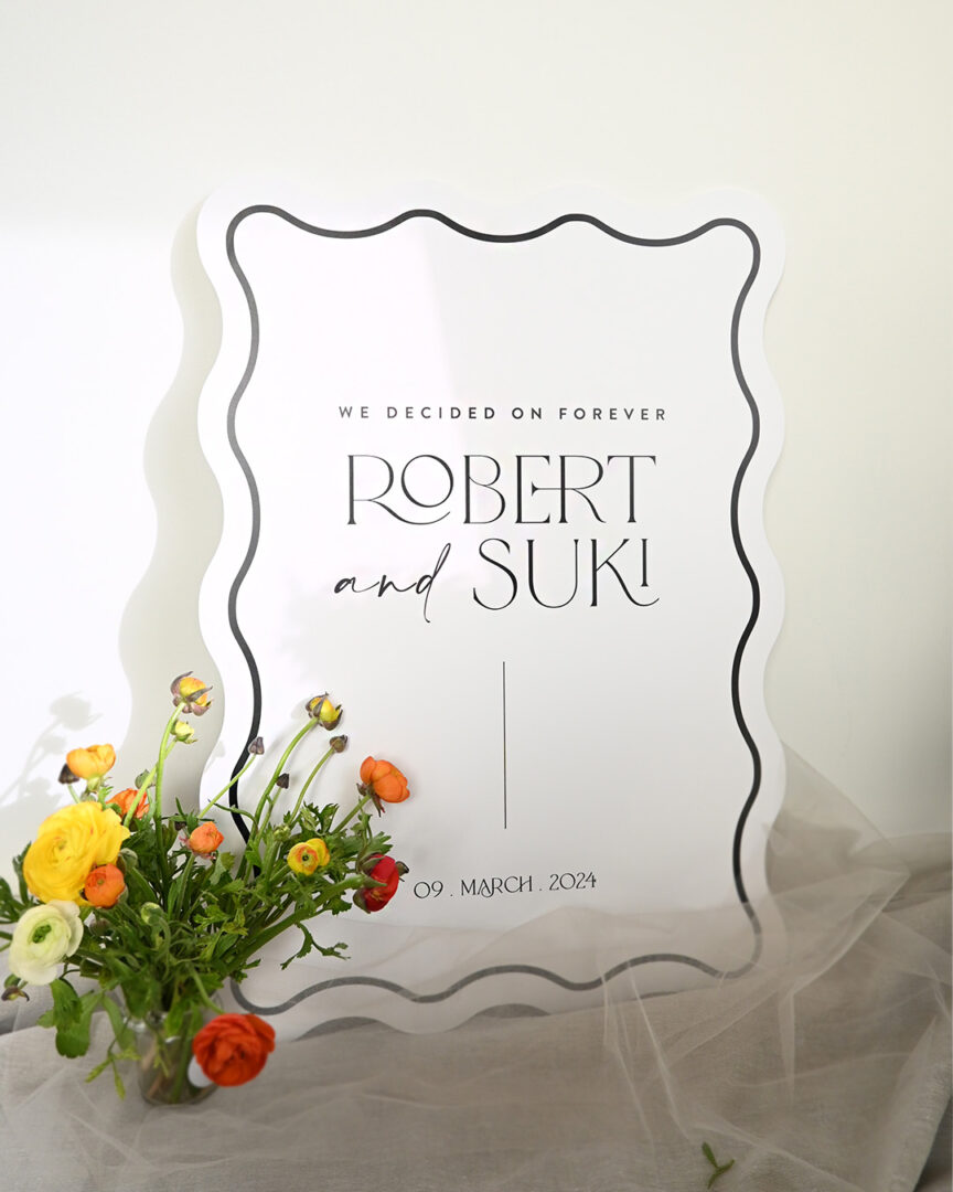Paperlust Grace wave-edge wedding welcome sign reading We Decided On Forever, Robert and Suki, on a wooden easel