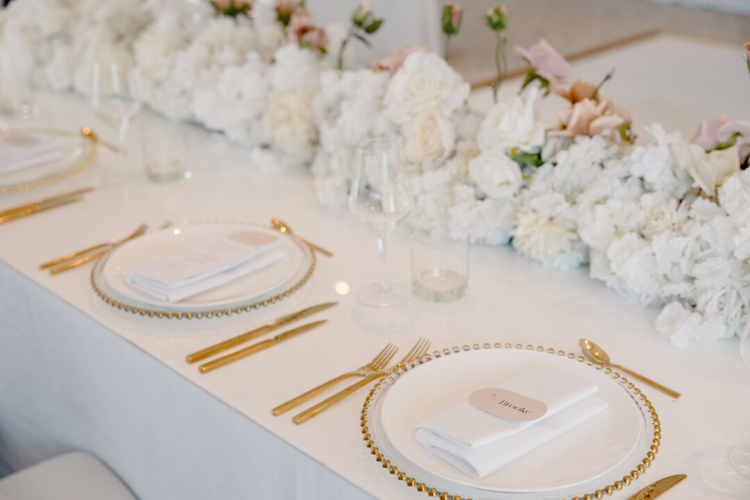 Wedding place cards on gold charger plates at elegantly set reception table