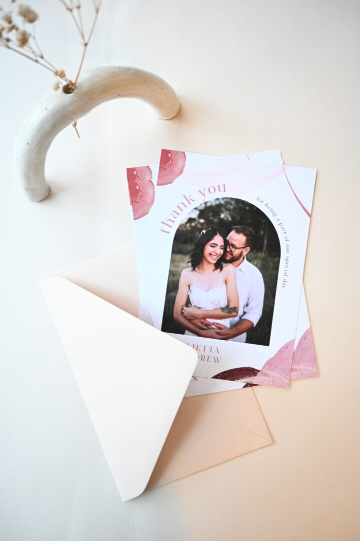 Paperlust Neapolitan wedding thank you card with pink watercolour arch photo, styled with envelopes and dried flowers