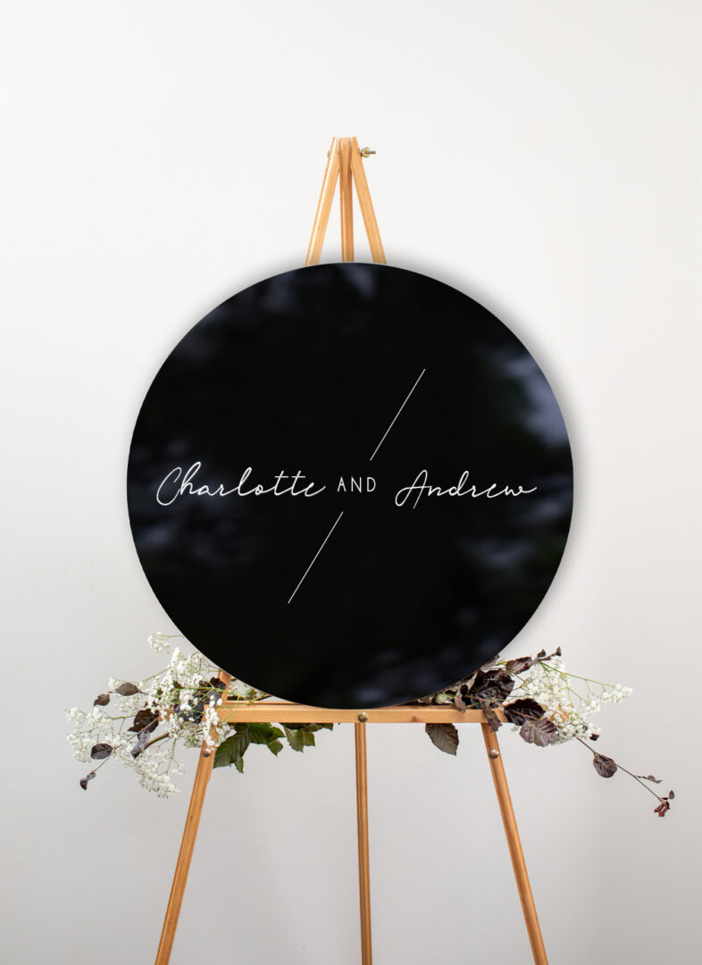 Round black acrylic wedding welcome sign on wooden easel