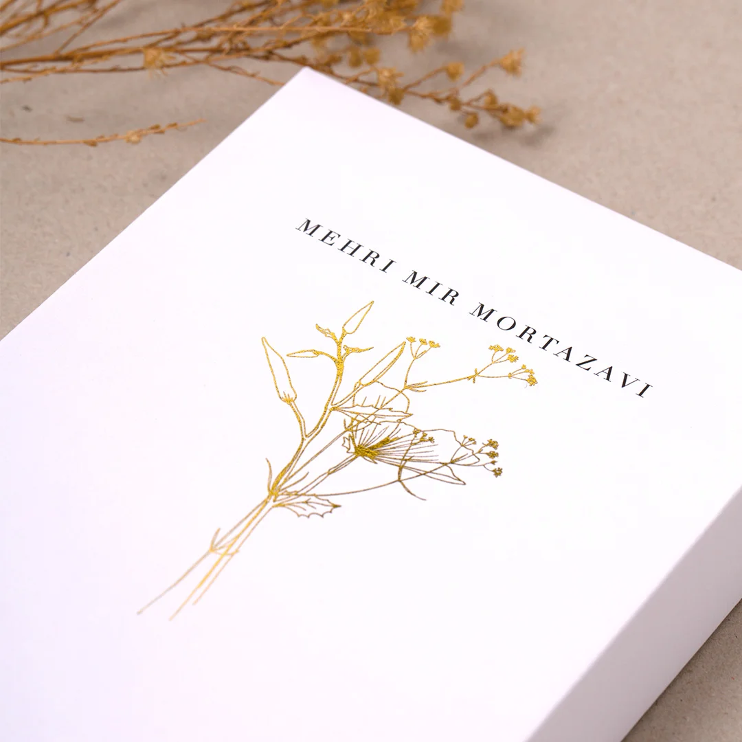 close-up of a gold-foil pressed anniversary card on cream heavyweight paper, shown open with handwriting inside, placed beside yellow roses on a marble surface wedding stationery