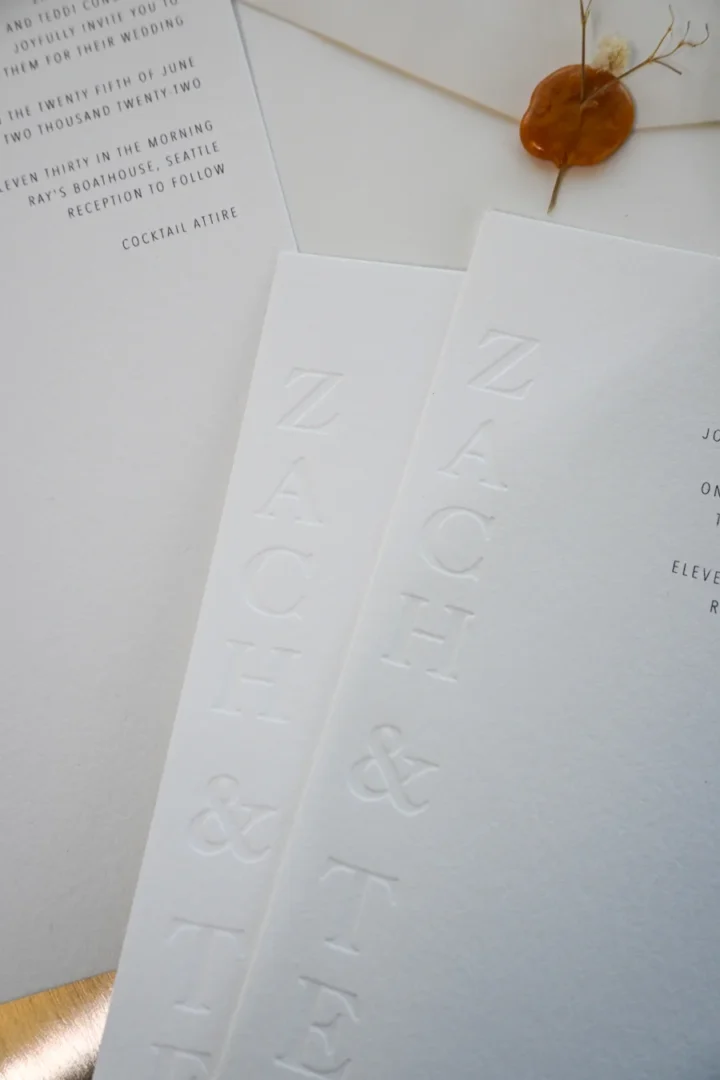 Close-up of a printed bridal shower invitation with flat gold foil lettering on a cream letterpress-textured stock, alongside matching envelope and gold wax seal, luxury stationery editorial wedding stationery