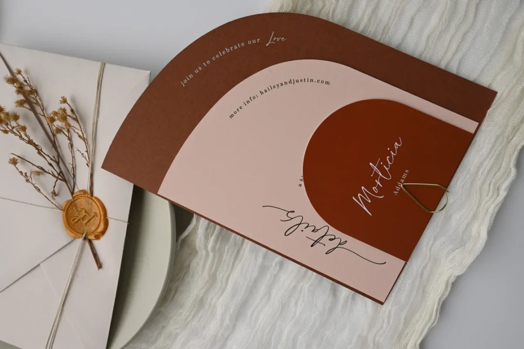 couple at a post office counter handing a sample sealed wedding invitation envelope to a postal clerk for weighing, warm in-store light wedding stationery