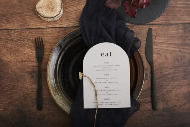 couple holding hands across a rustic wooden table set for an anniversary dinner, warm candlelight, engraved wooden keepsake box in the foreground wedding stationery