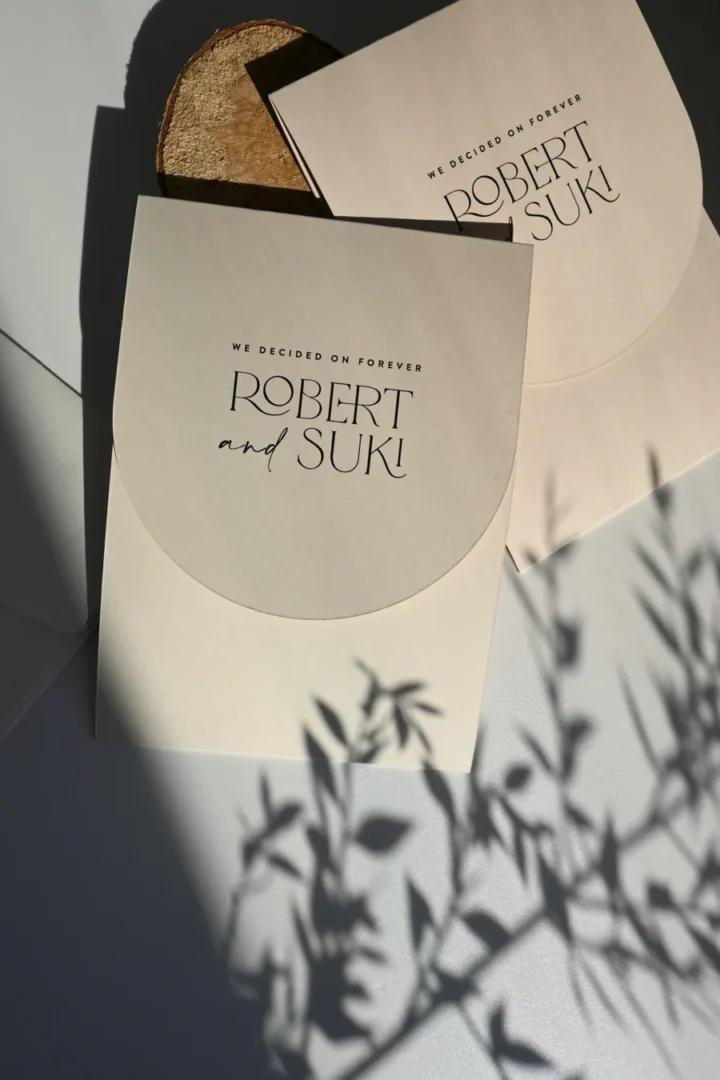couple sitting across a table from their wedding photographer reviewing a printed portfolio book in a bright airy studio wedding stationery