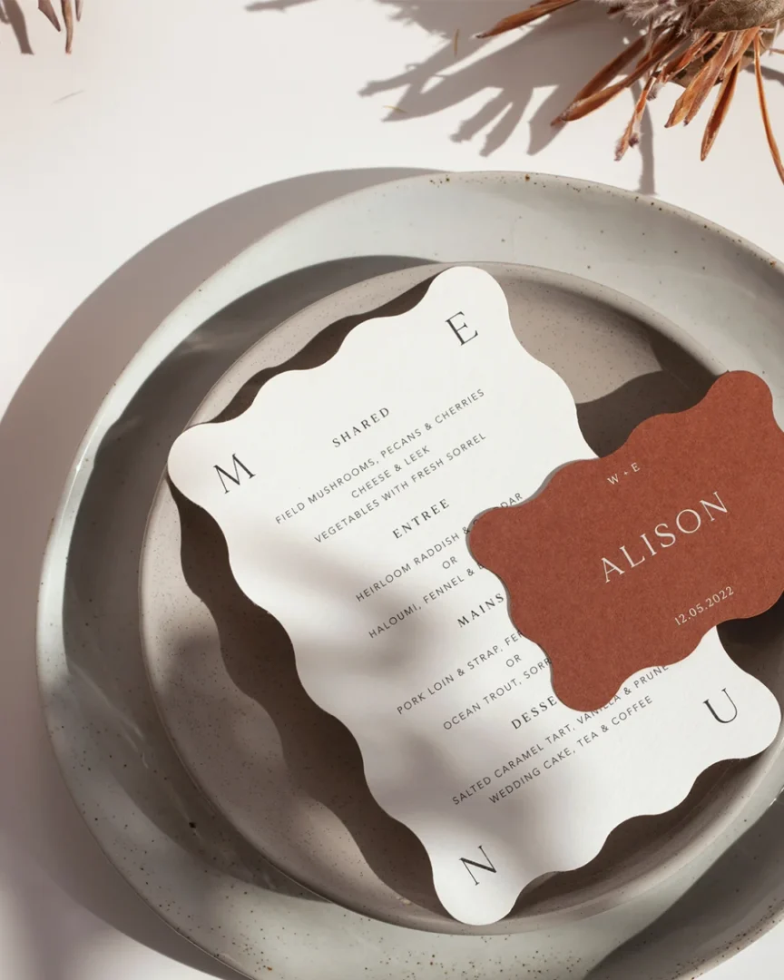 Elegantly styled table for a shower event featuring a round menu card, styled place card, and warm neutral tableware on a wooden surface, well-lit product lifestyle shot wedding stationery