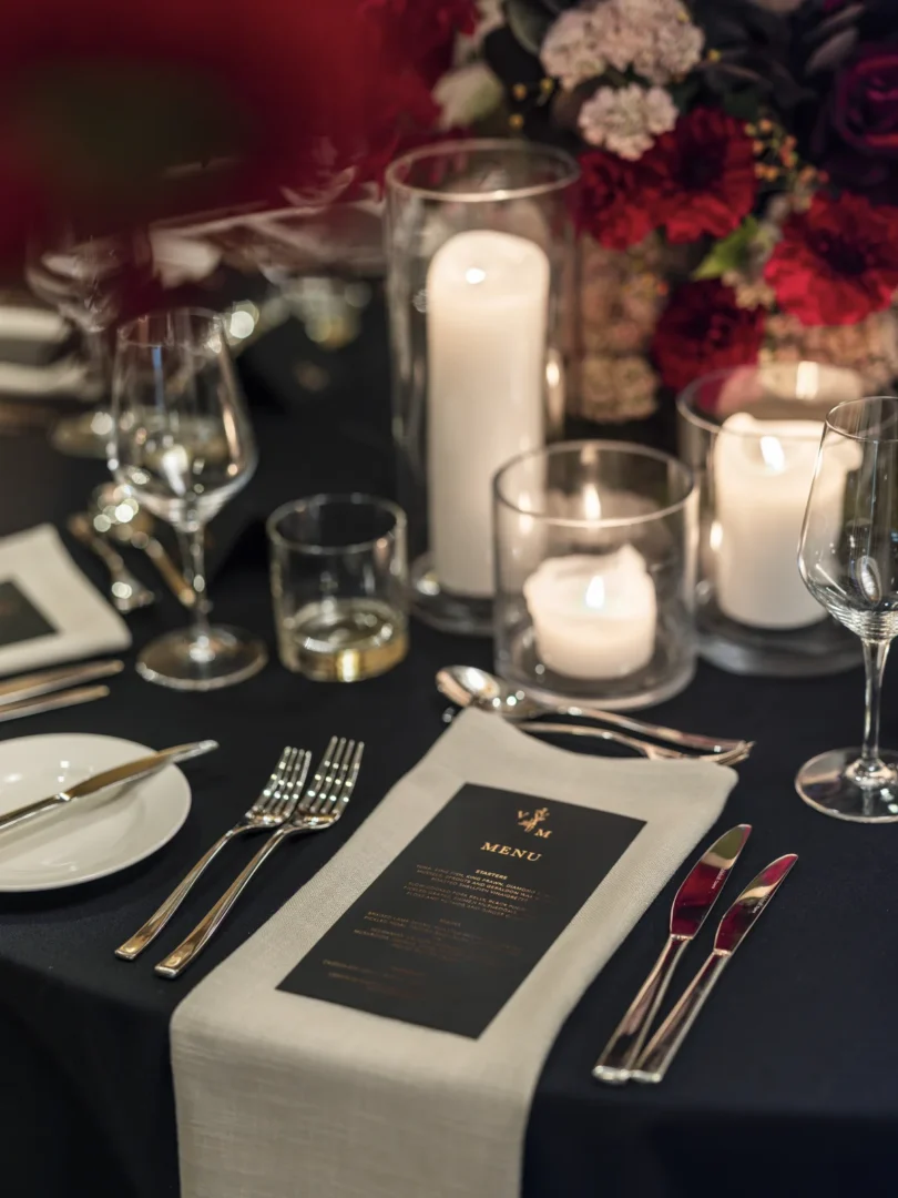 golden anniversary table centerpiece with yellow roses, gold pillar candles, and champagne flutes arranged on a white linen tablecloth wedding stationery