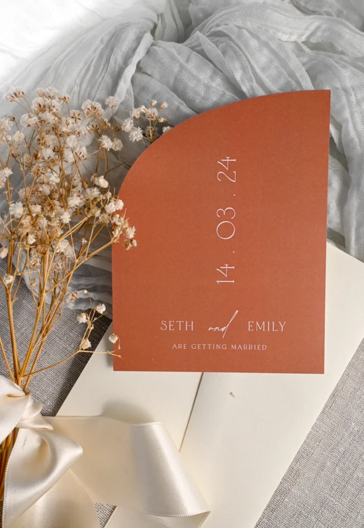 personalized anniversary card with elegant gold foil lettering on white stock, flat lay on marble surface with small flowers and ribbon wedding stationery