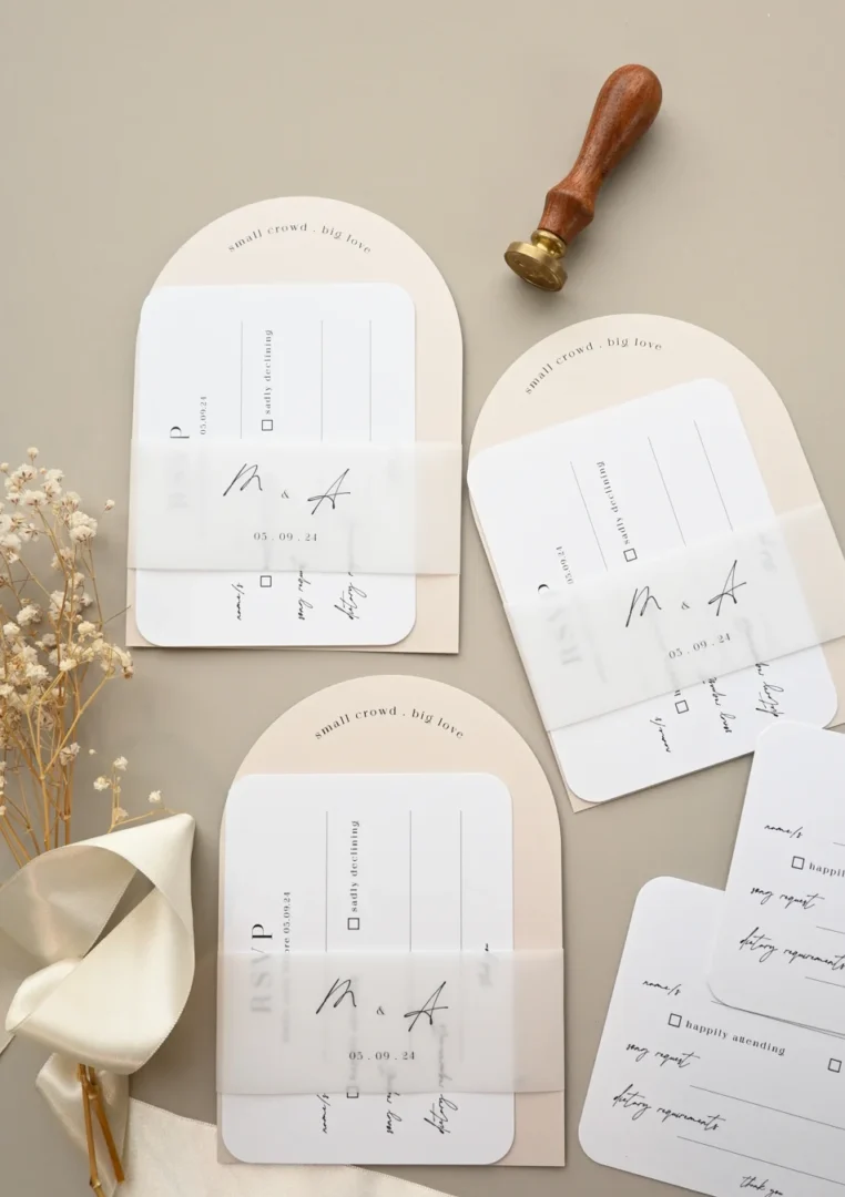 Wedding stationery suite flatlay in blush pink and black color palette - invitation, RSVP card, and envelope displayed on white marble surface, modern typography, horizontal composition wedding stationery