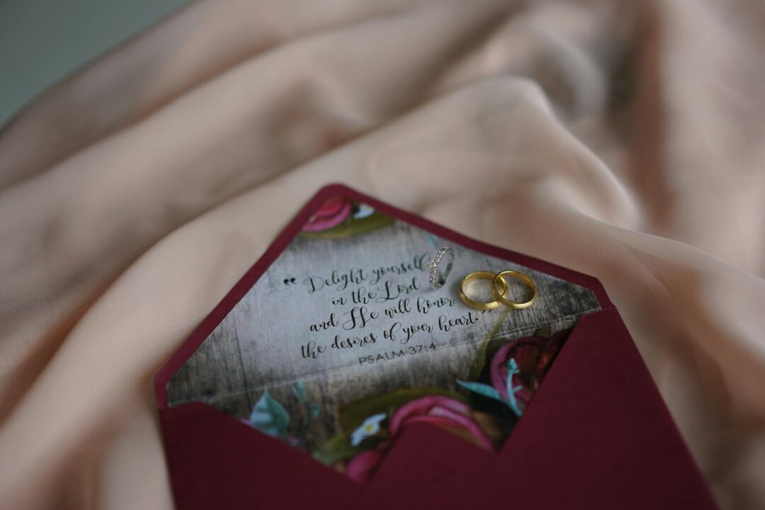 Elegant burgundy and gold wedding suite display with RSVP card, invitation, and information card on a styled tabletop with gold leaf props a