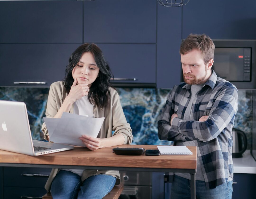 couple at laptop reviewing wedding budget spreadsheet together, warm home setting