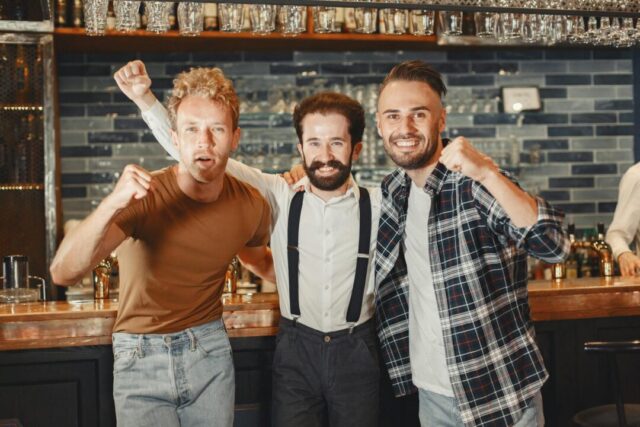 group of groomsmen celebrating at a rooftop bar, laughing and raising glasses, golden hour lighting, city skyline background