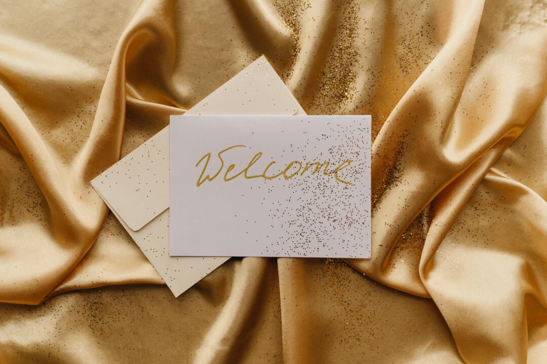 Paperlust invitation suite flatlay with gold flat foil detail on cream card, styled with champagne flutes and a gold ribbon, Paperlust Drive