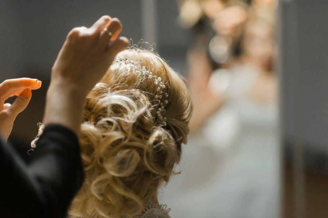 Bride in a low updo with pearl-tipped hairpins scattered through the style, photographed from behind to show the full arrangement of pins ag
