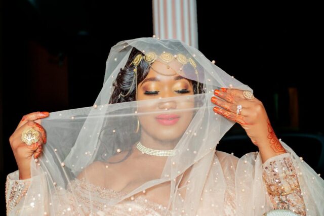 radiant bride with soft-glam bridal makeup, dewy skin and delicate lashes, seated at a dressing-room mirror in a white wedding dress