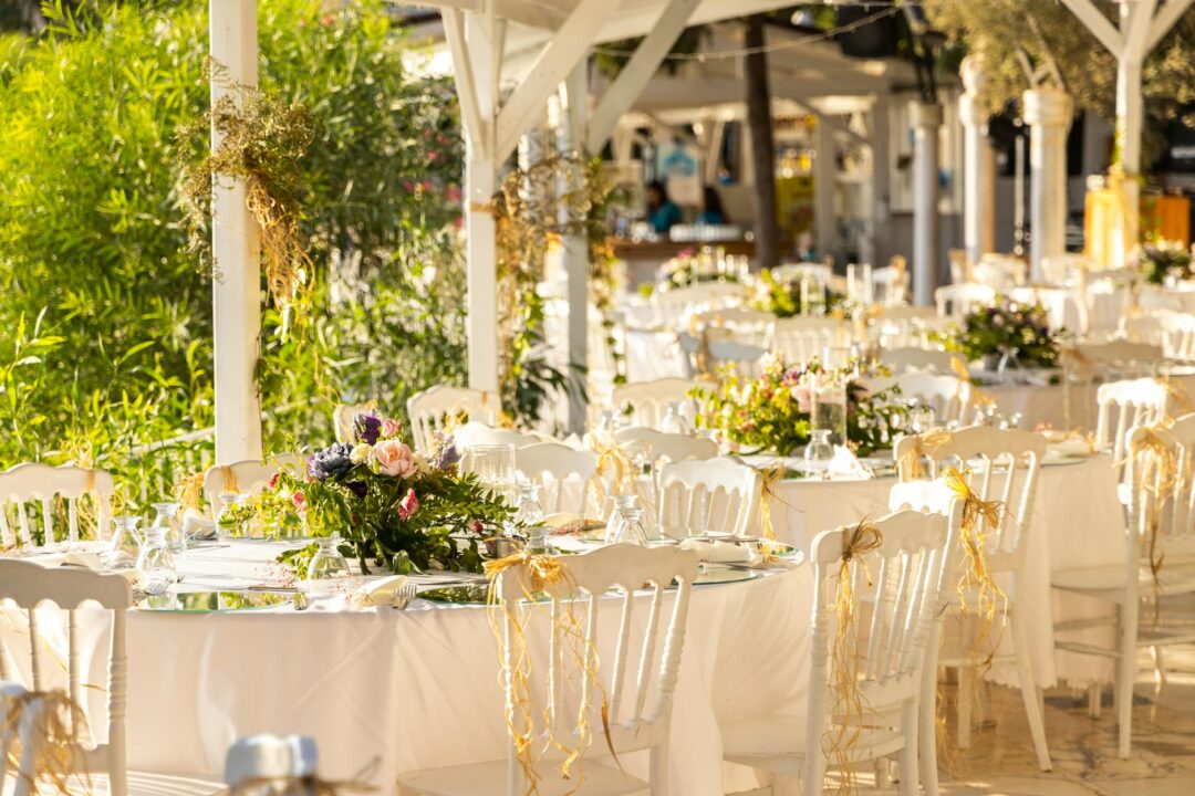 elegant outdoor daytime wedding reception tables with floral centerpieces, white linens, and natural sunlight through garden trees