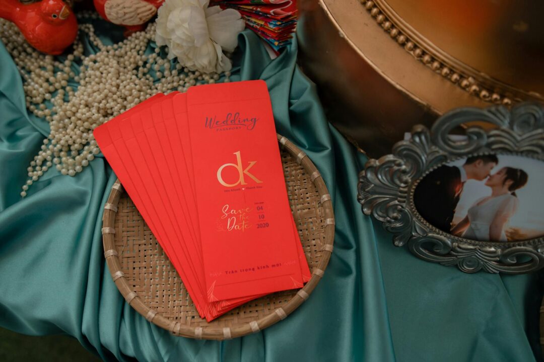 Elegant red and gold Chinese wedding invitation suite flatlay with matching envelope, red ribbon, and gold double happiness seal on a cream surface