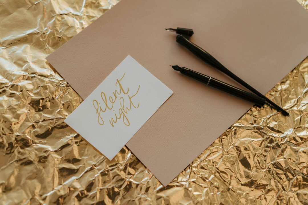 Close-up of a printed Paperlust note card with gold flat foil text resting inside a kraft welcome bag with tissue paper, alongside a small s
