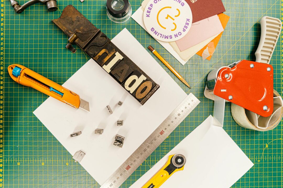A crafting workspace with hand tools, metal type blocks, coloured cardstock and a green cutting mat.