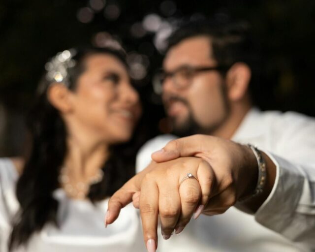 romantic close-up of newly engaged couple holding hands showing sparkling engagement ring, warm natural light, celebratory atmosphere