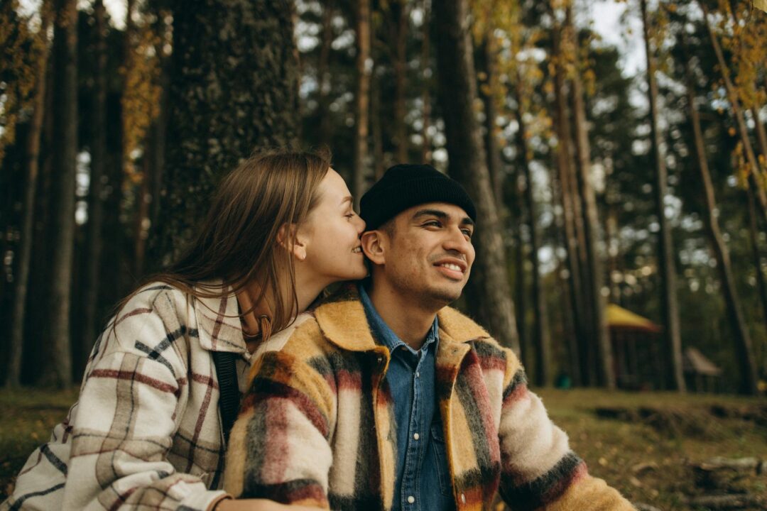 couple in autumn forest setting, warm golden hour light through fall foliage, cozy knitwear outfit pairing