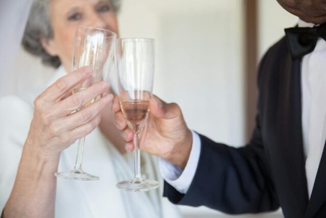 a father in a navy suit raising a champagne glass in a toast at an elegant wedding reception, his daughter the bride smiling warmly beside him, soft golden candlelight in the background
