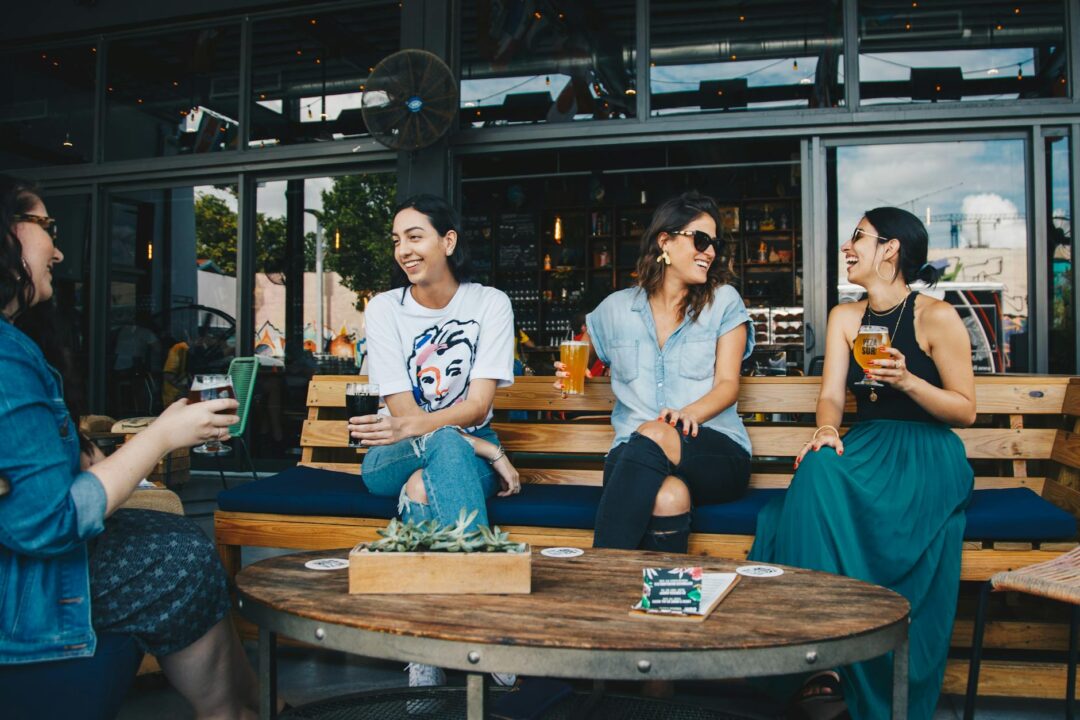 outdoor hens party group of friends laughing with cocktails at an Australian beach or vineyard setting, candid golden-hour shot, colourful d