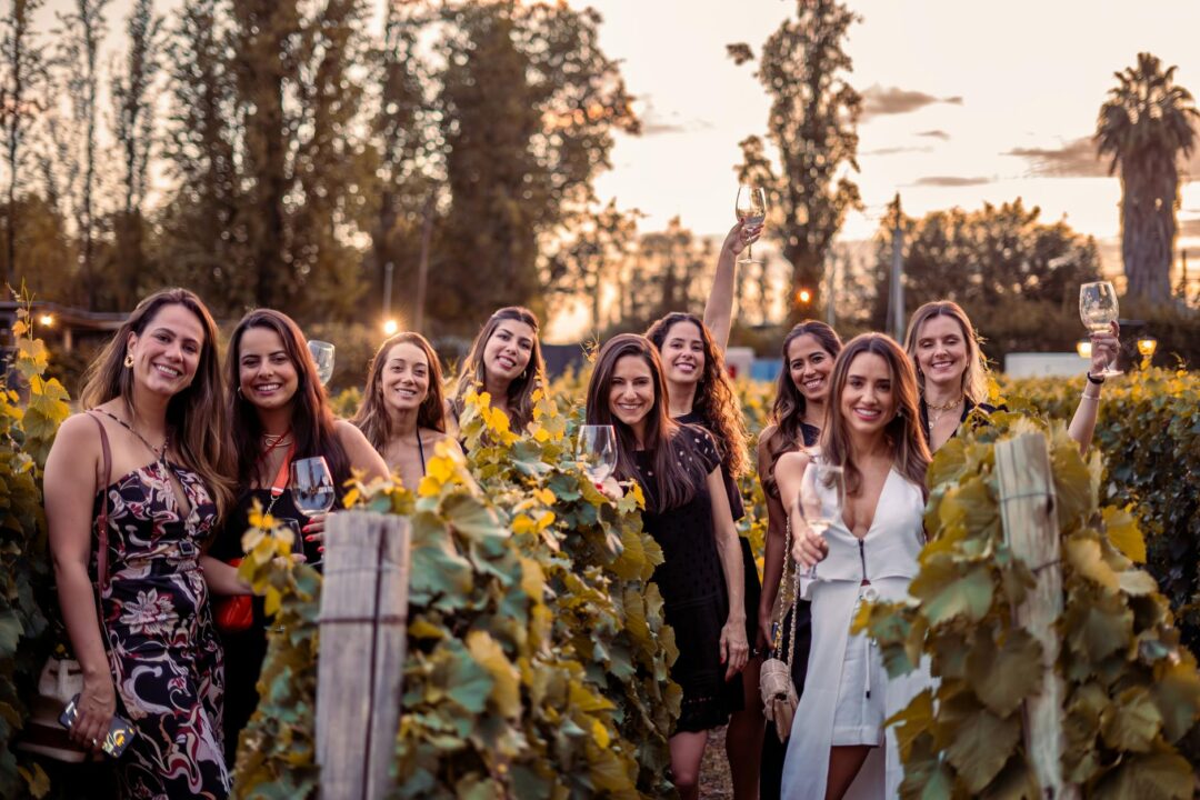 group of women at a vineyard hens party, laughing around a picnic grazing board with wine glasses, boho styling with dried florals and terra