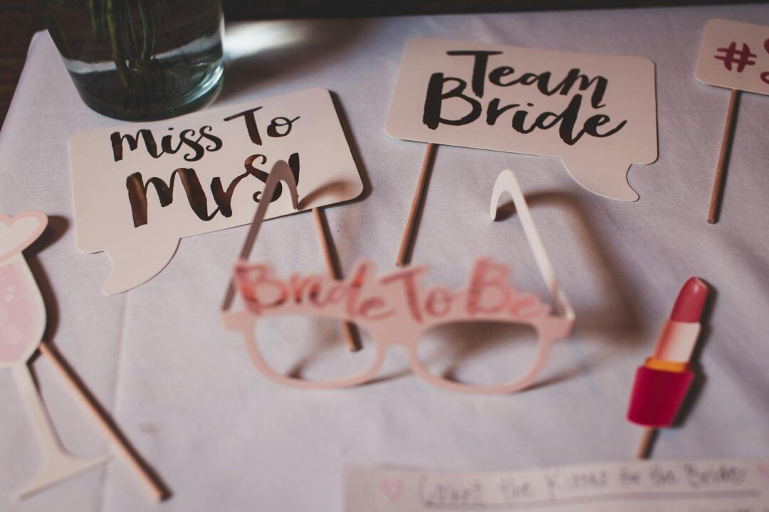 flat lay of hens party decorations and custom hens night invitations with sashes, balloons and florals, styled on a marble surface, boho-gla