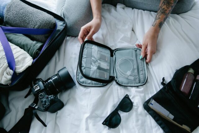 open suitcase styled flatlay with honeymoon essentials, sunscreen, sunglasses, passport, swimwear, white flowy dress, marriage certificate v