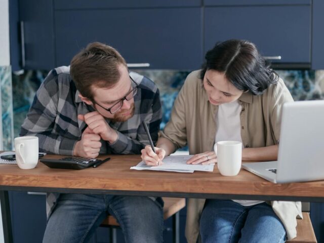 couple reviewing wedding budget spreadsheet together at kitchen table, invitation samples on the table