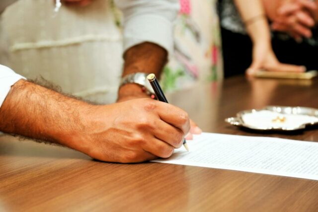 person writing a wedding speech at a desk with wedding planning aesthetic, laptop open, engagement ring visible, notebook, pen, warm natural