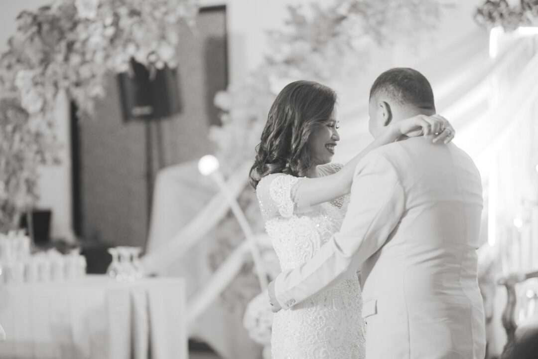 bride and groom sharing a quiet moment at their reception, champagne glasses visible, wedding programs on the table behind them