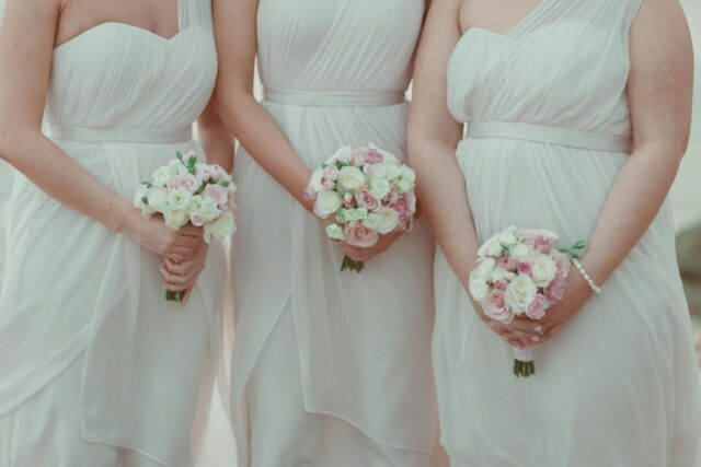 Bridesmaids in soft pastel dresses holding pink and white bouquets at an outdoor wedding, capturing the maid of honor