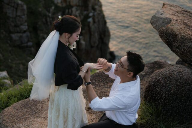 couple sharing an emotional proposal moment outdoors at golden hour, one partner kneeling with ring box, surrounded by soft natural light
