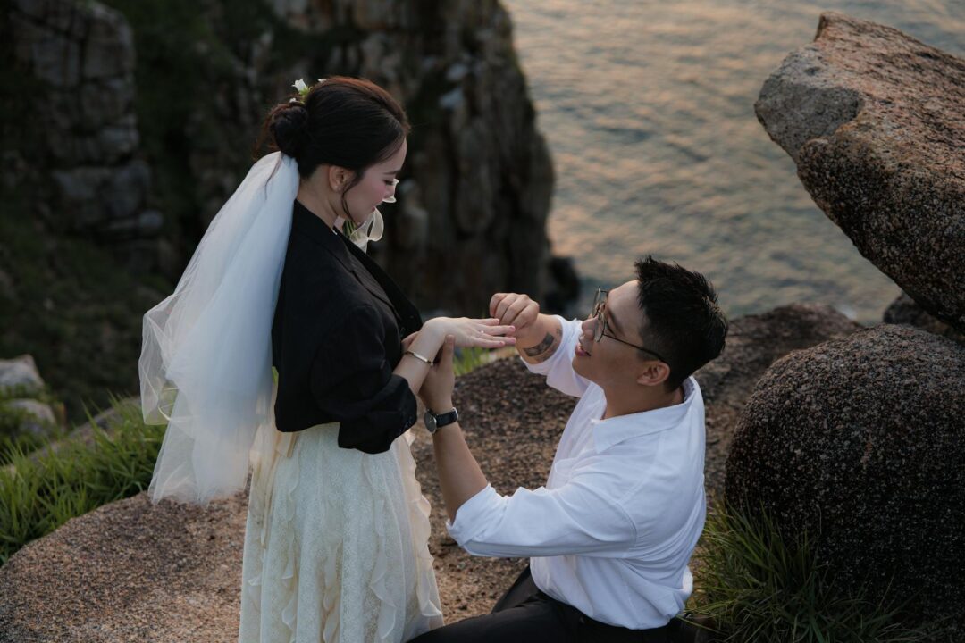 couple sharing an emotional proposal moment outdoors at golden hour, one partner kneeling with ring box, surrounded by soft natural light