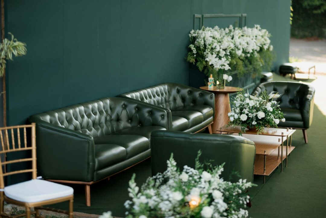 Modern wedding reception lounge zone with low velvet seating, a marble side table, and pendant cluster lighting overhead, styled in a jewel-