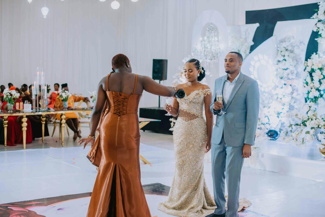 mother of the groom standing at wedding reception podium, champagne glass raised, warm smile, elegant venue with guests in background
