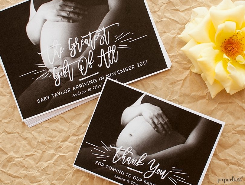 Two Paperlust landscape birth announcement cards featuring a black-and-white maternity photo with handwritten-style white script, addressed kraft envelopes ready to mail