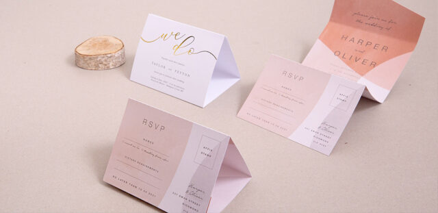Paperlust coral wedding invitation suite -- folded coral and peach RSVP cards with gold foil 'we do' on a soft beige surface, blush ombre details