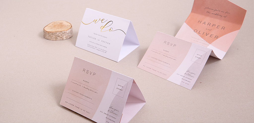 Paperlust coral wedding invitation suite , folded coral and peach RSVP cards with gold foil 'we do' on a soft beige surface, blush ombre details