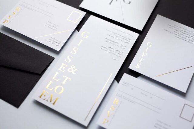 Paperlust oversized statement wedding invitation -- tall portrait white card with vertical gold foil typography spelling couple names, premium editorial format, paired with black envelope and matching RSVP and gifts cards