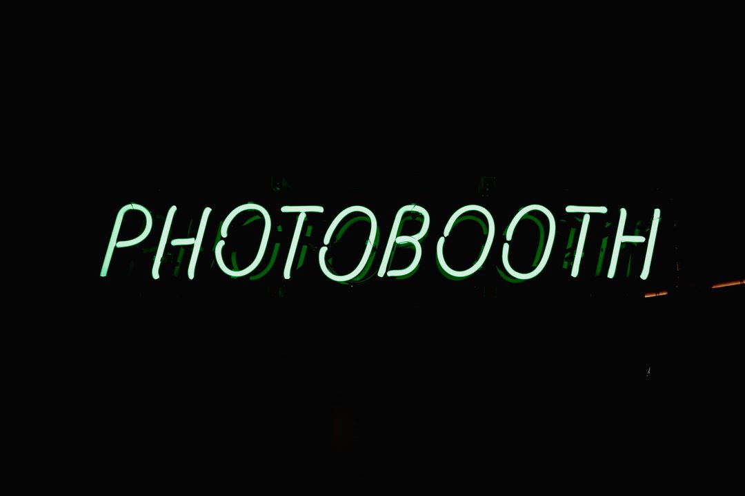 Green neon photo booth sign glowing against a dark wall at a wedding reception