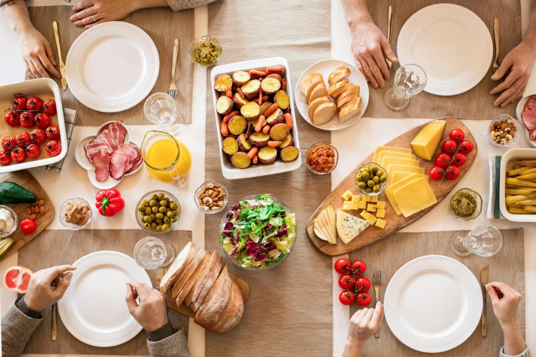 family-style wedding dinner with shared platters of food on a rustic wooden farm table, wildflowers in bud vases, warm evening light, guests