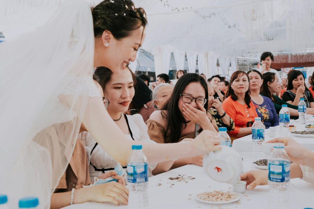 wedding reception guests serving themselves at a beautifully decorated buffet table with floral centerpieces and elegant table signage, soft
