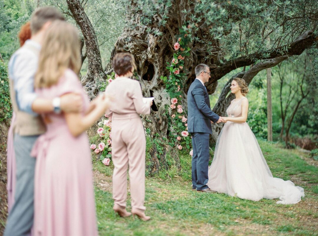 couple at outdoor ceremony exchanging modern vows, bright natural light, garden or vineyard backdrop, both partners smiling through emotion, candid au