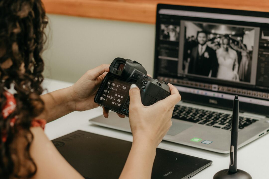 couple sitting across a table from a wedding videographer reviewing footage on a laptop in a bright modern studio, camera equipment visible in backgro